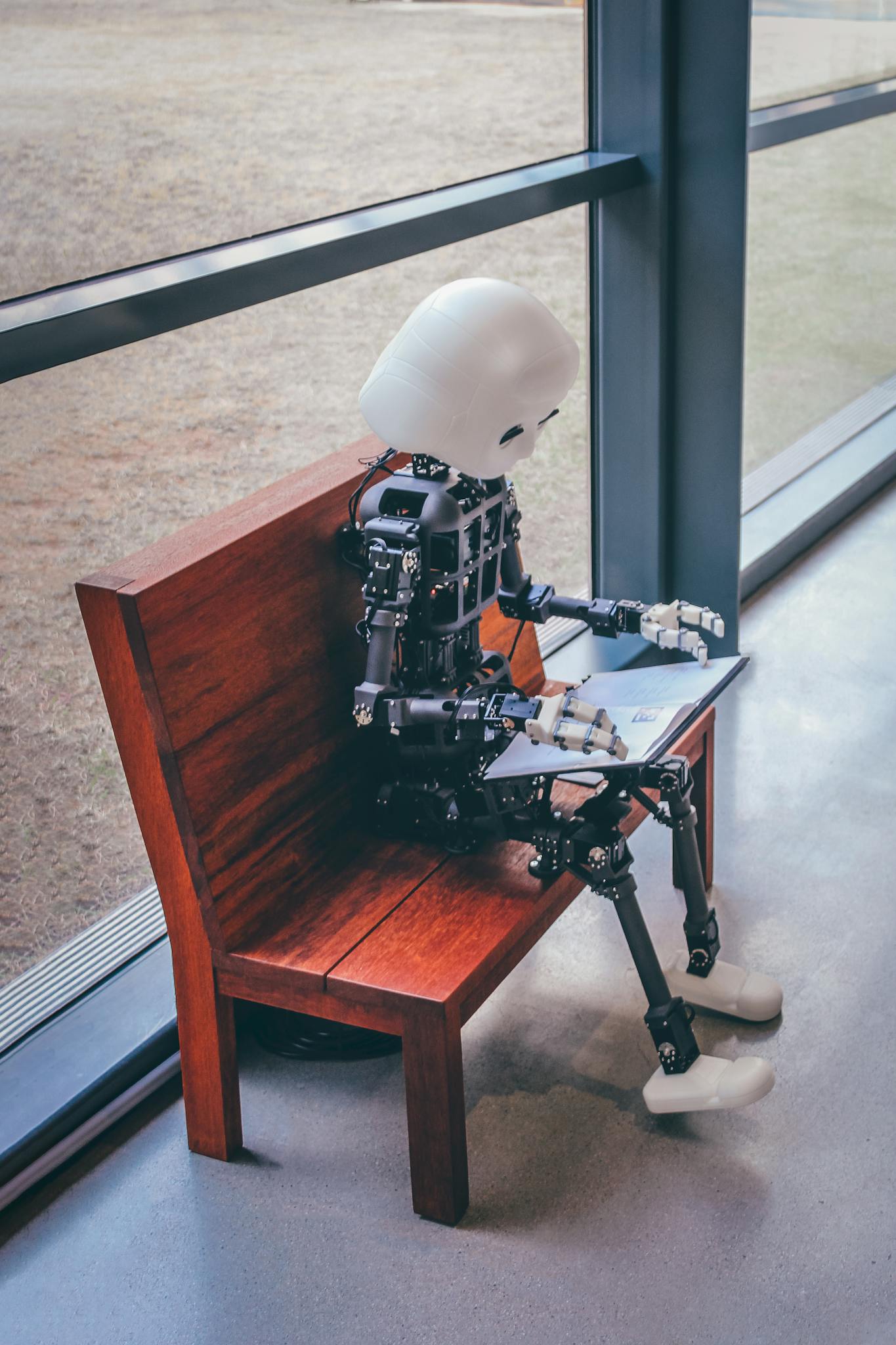 A humanoid robot sits on a wooden bench, reading in a modern setting in Seoul.